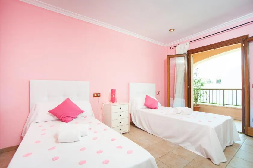 A pink bedroom with two single beds and an open balcony door.