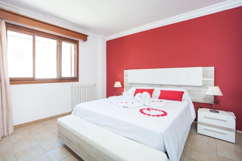 A bedroom with a bed dressed in white against a red accent wall.