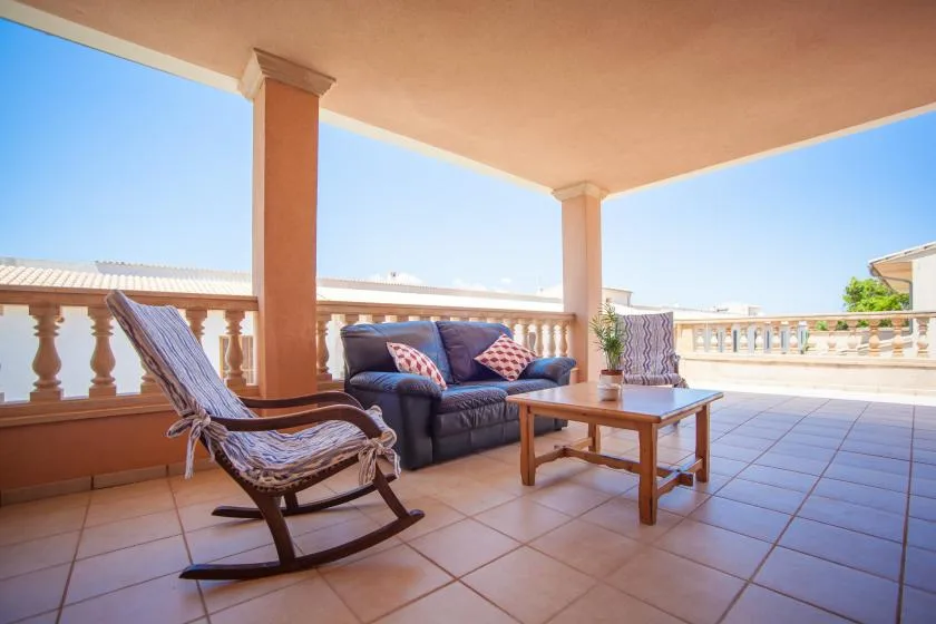 A covered terrace with seating and a low table overlooks a bright open view.