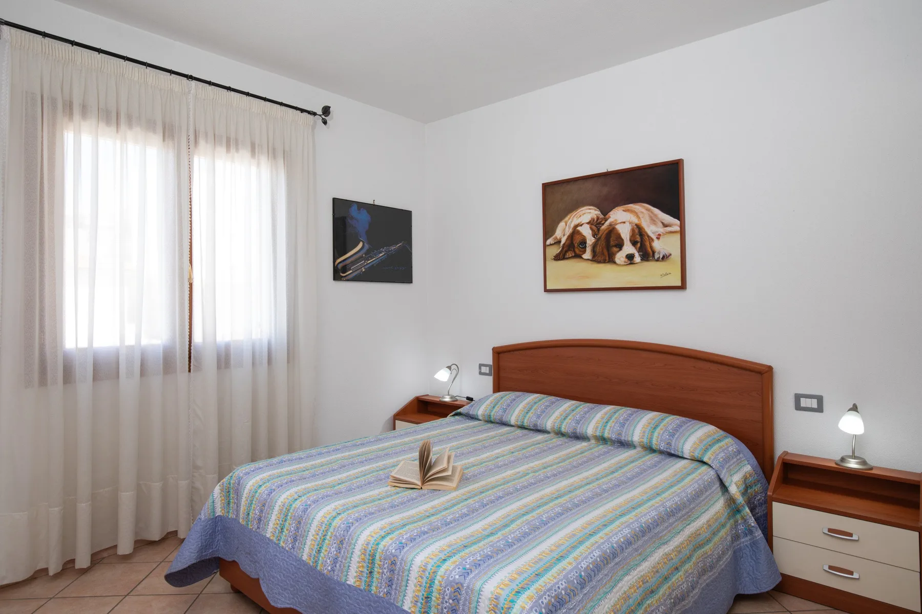 Un dormitorio con una cama cubierta por una colcha a rayas y una ventana con cortinas.