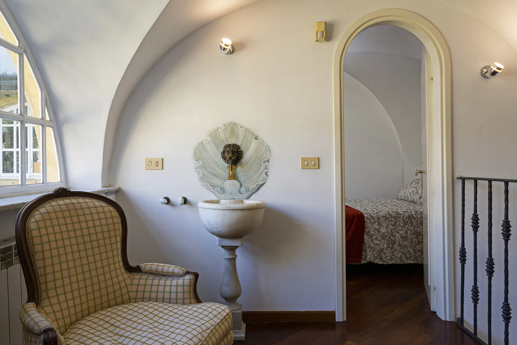 A curved interior sitting area with a patterned chair and decorative wall fountain.