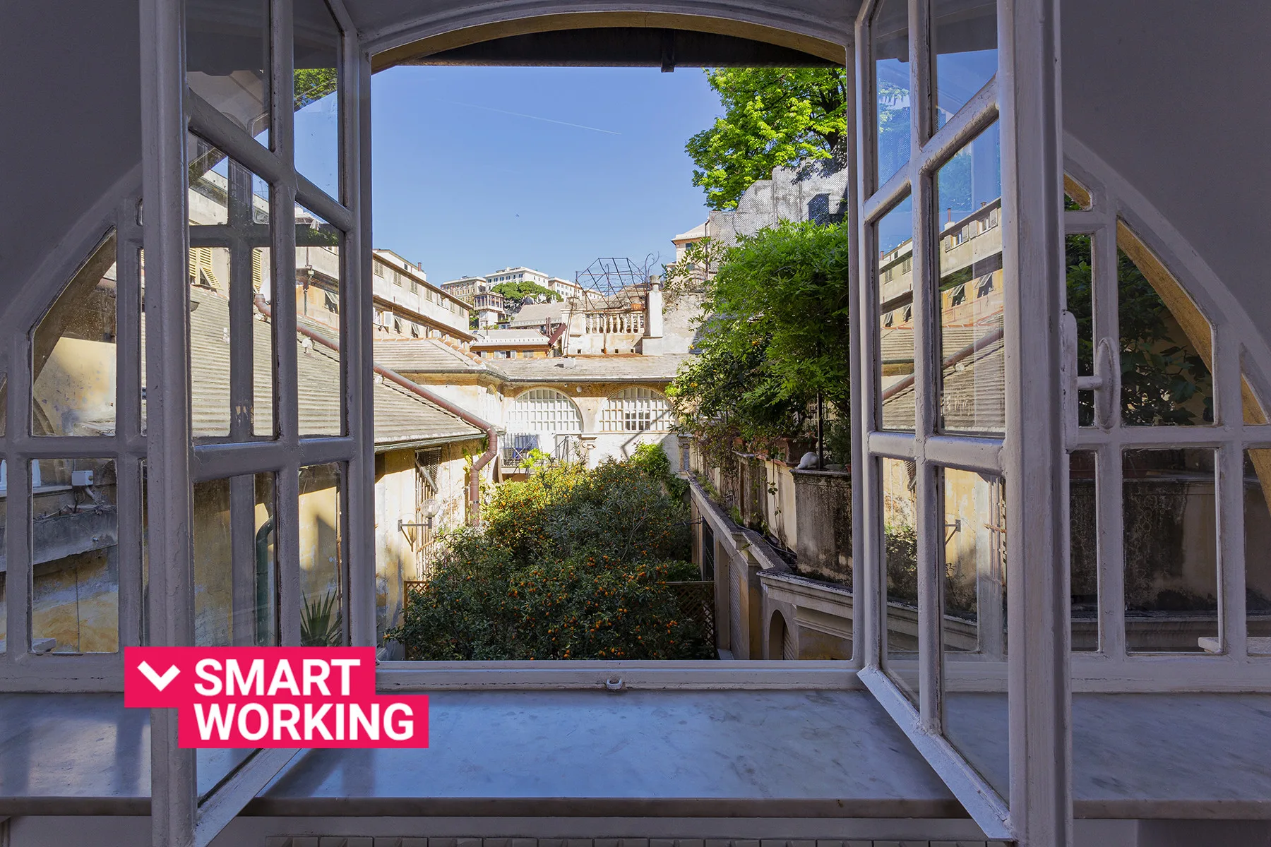 An open window overlooks a courtyard with greenery and surrounding buildings.