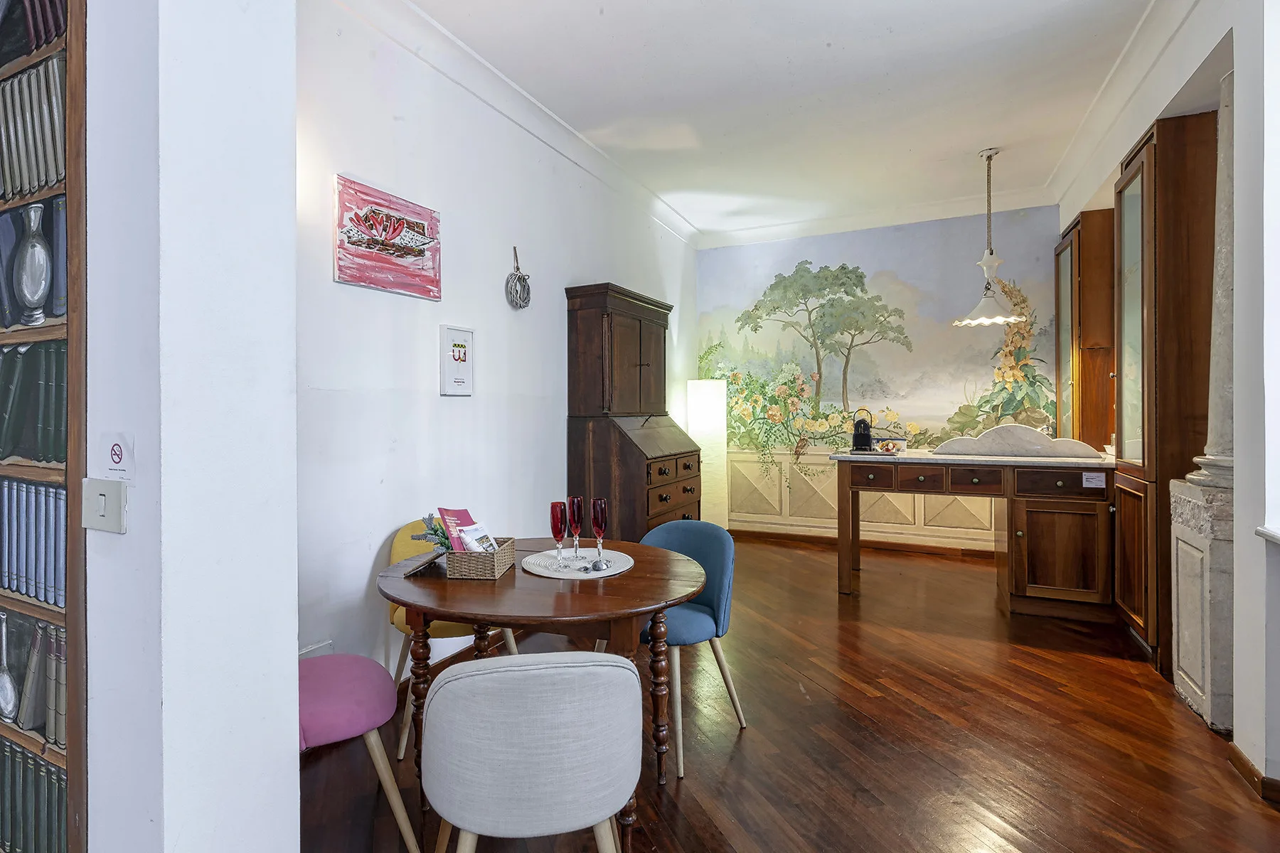 A furnished room with a round dining table and a painted landscape mural.