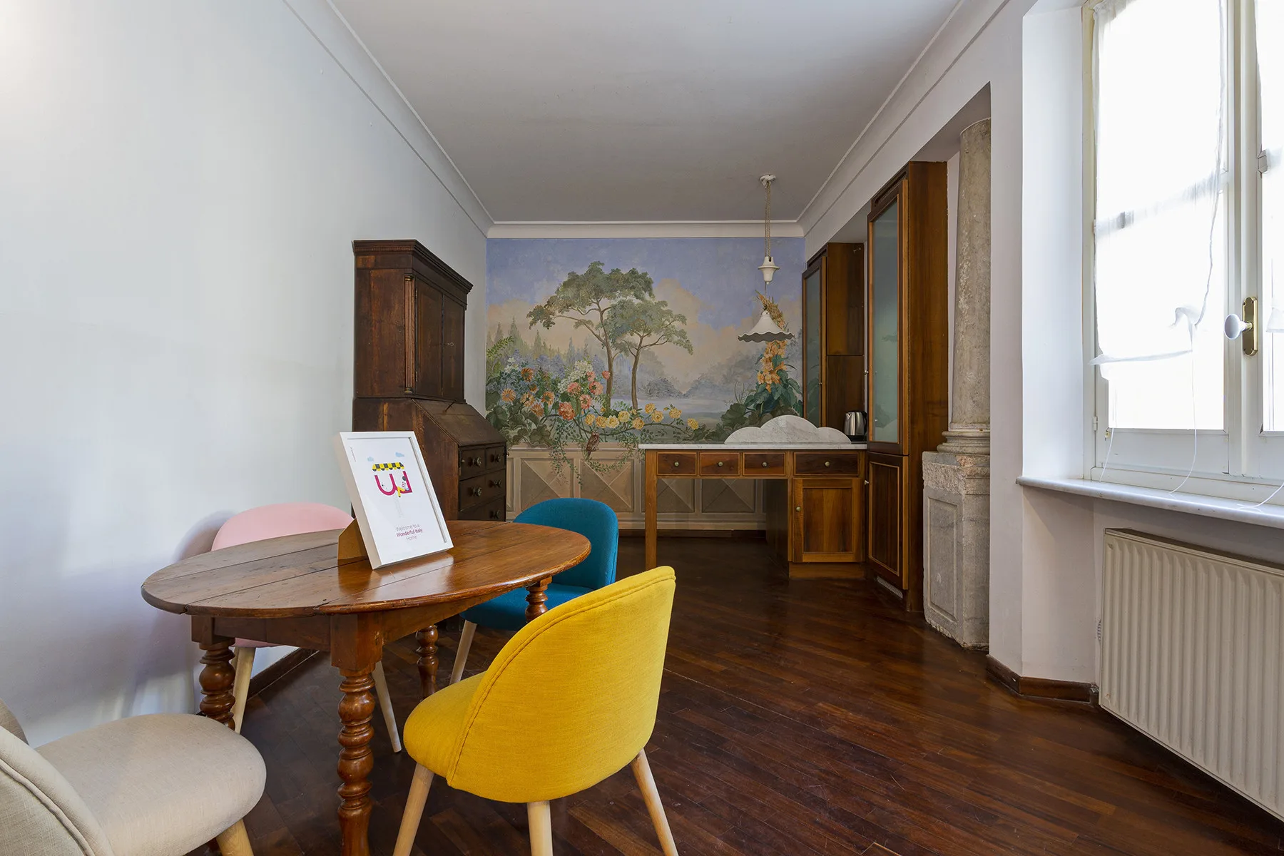 A dining room with a wooden table and a painted landscape mural.