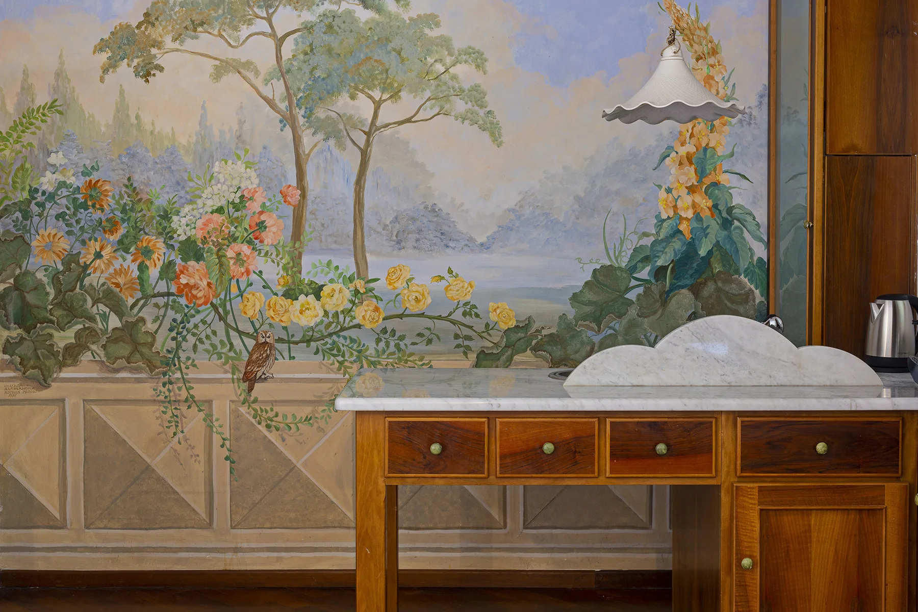 A washbasin sits beneath a large floral landscape mural, with wooden cabinetry below.