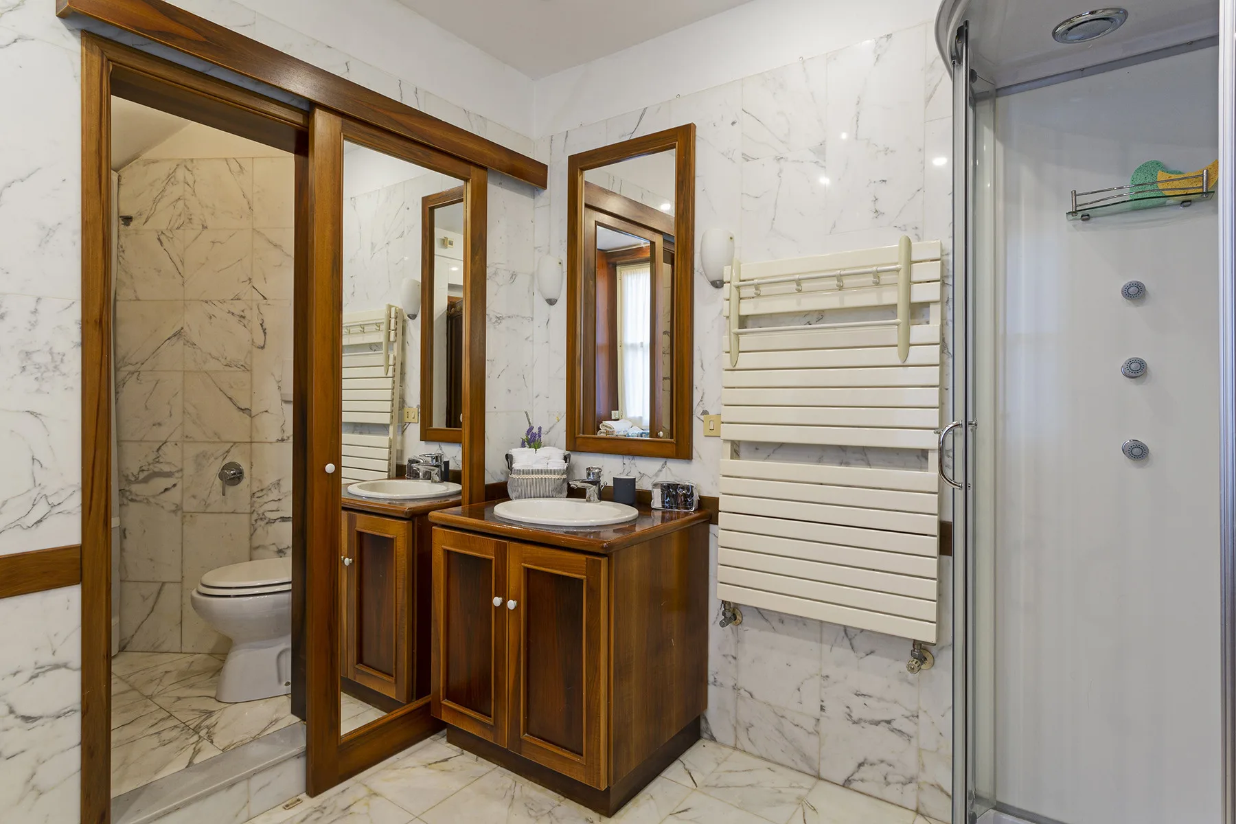 A marble bathroom with wooden vanity cabinets, a towel rack, and a glass shower.
