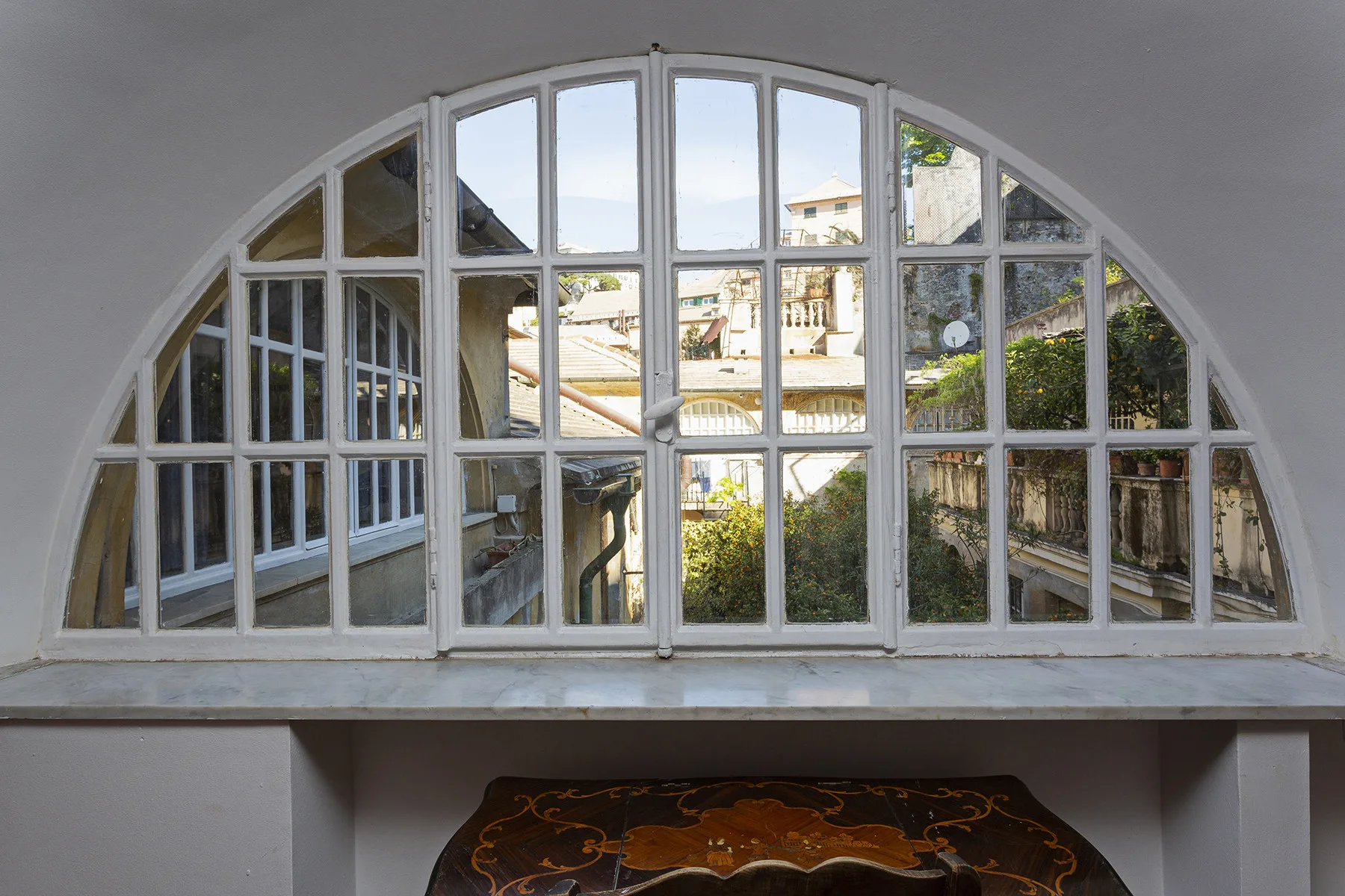 An arched window overlooks nearby buildings and greenery.
