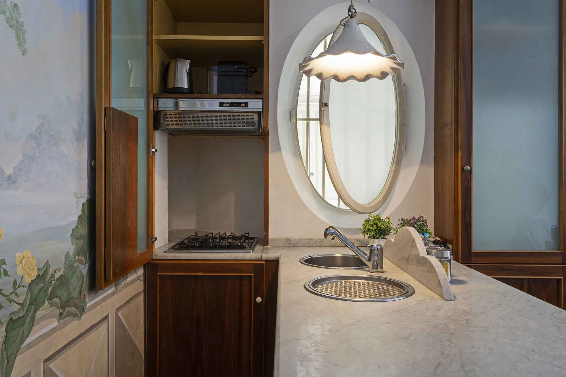 A compact kitchen counter with a sink, cooktop, and oval mirror.