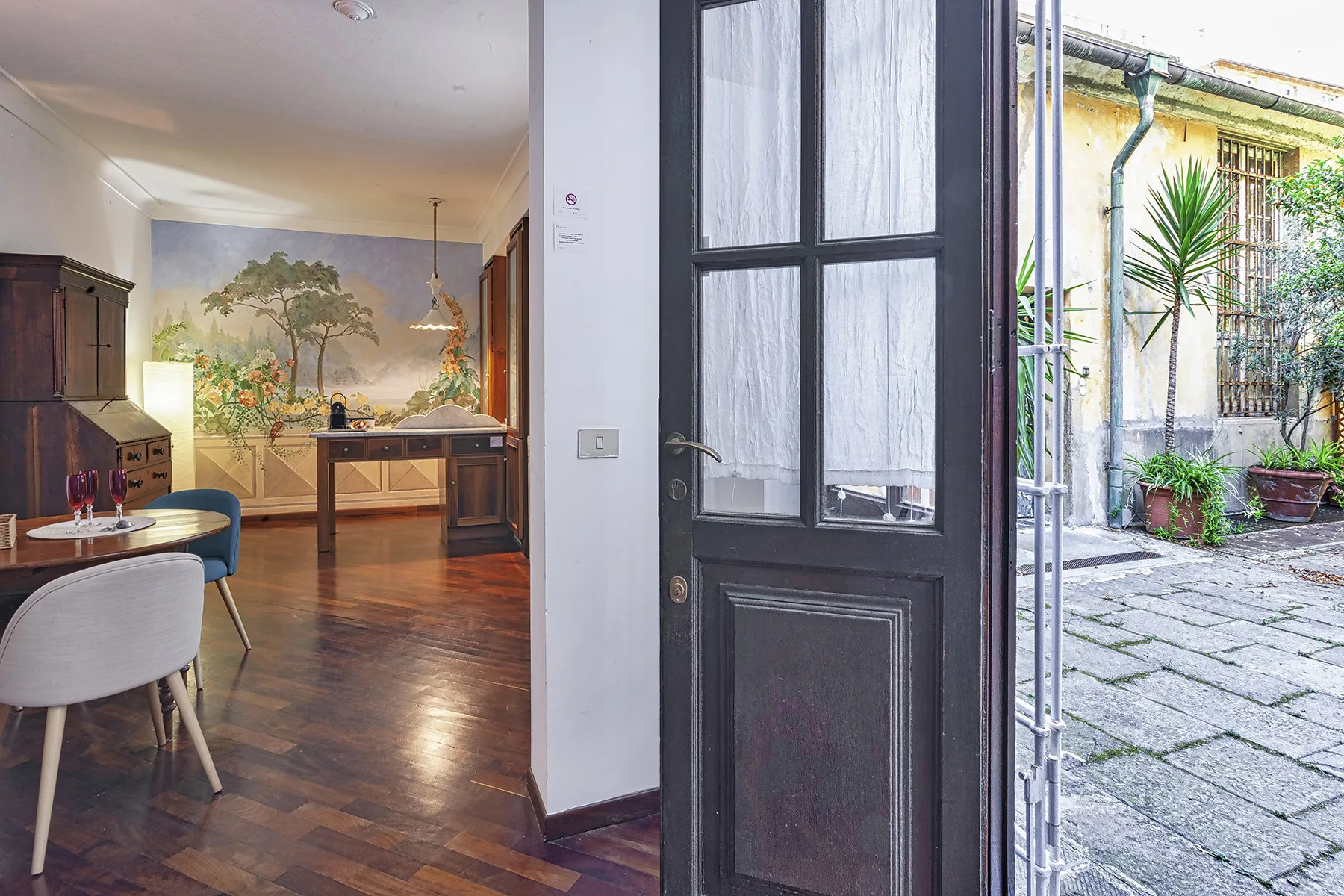 A dining room with a wooden table and chairs beside an open doorway to a courtyard.