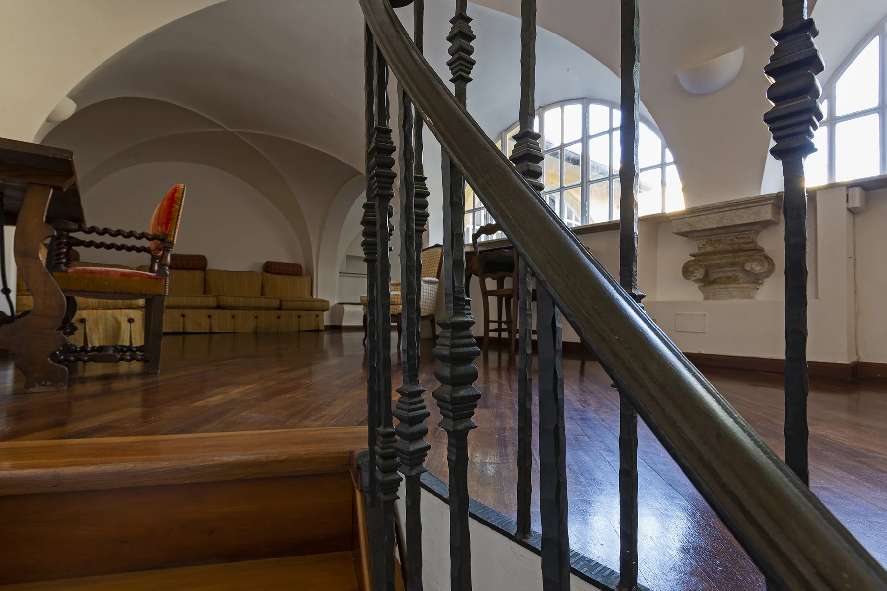 A wood-floored room with arched windows and a dark decorative railing.
