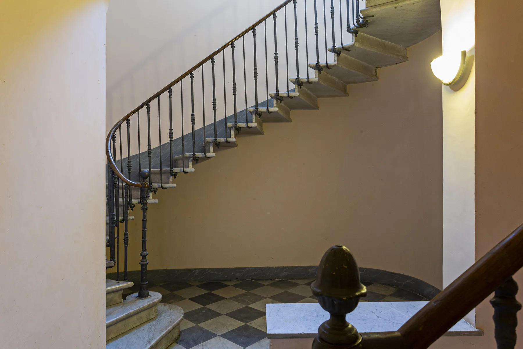An interior staircase with a curved metal railing above a checkered floor.