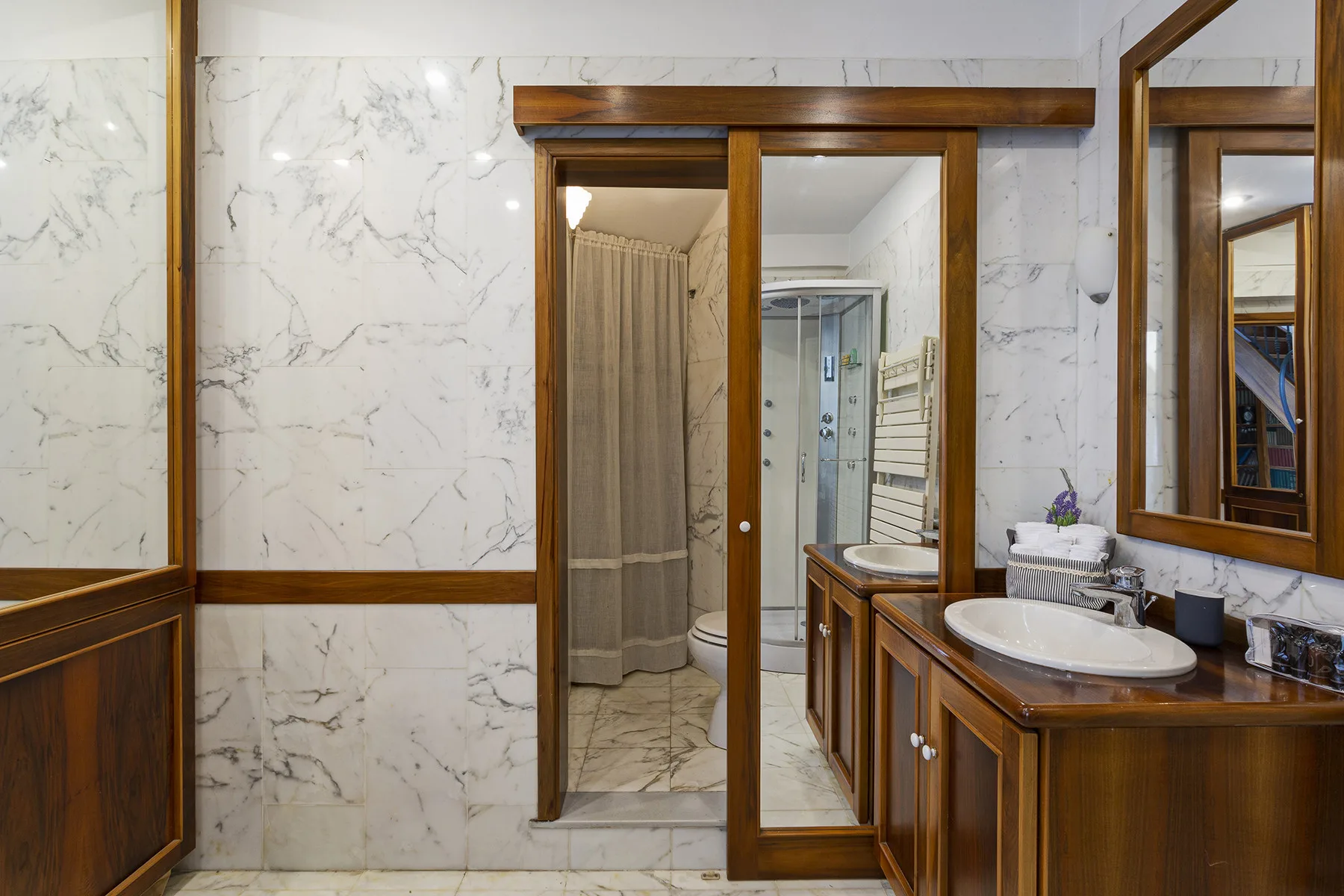 A marble bathroom with a wooden vanity and a glass shower.