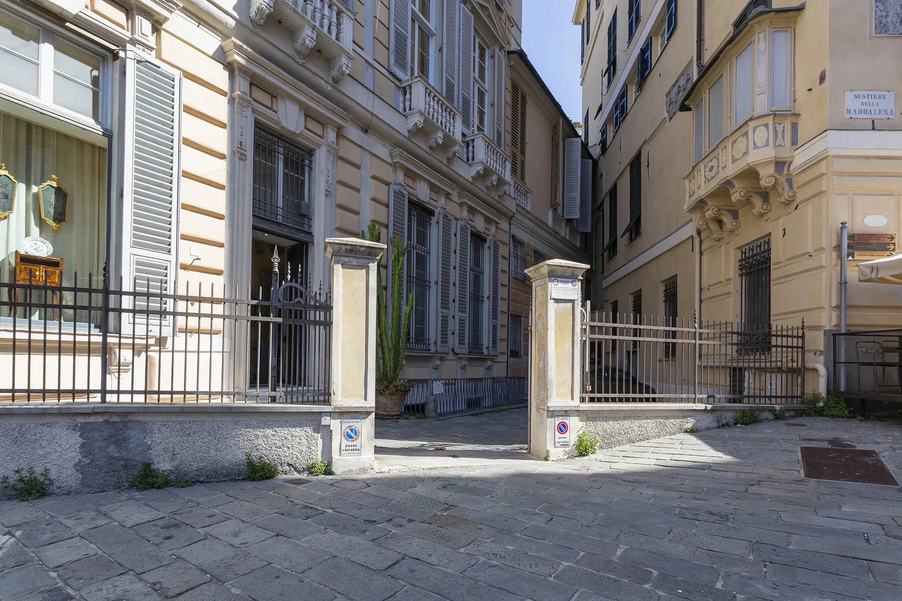 A stone-paved courtyard between tall city buildings, with metal railings along the entrance.
