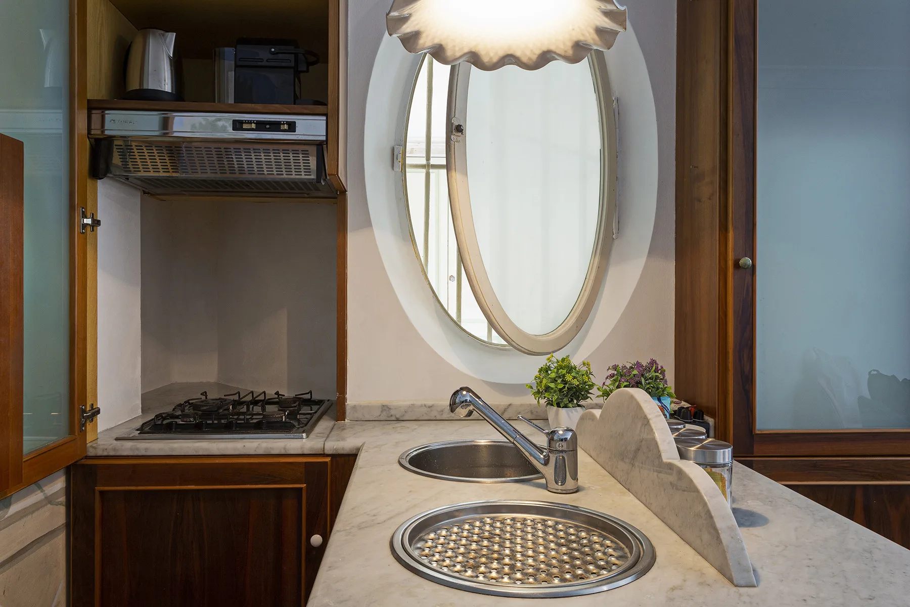 A kitchen counter with a sink, cooktop, and oval mirror.