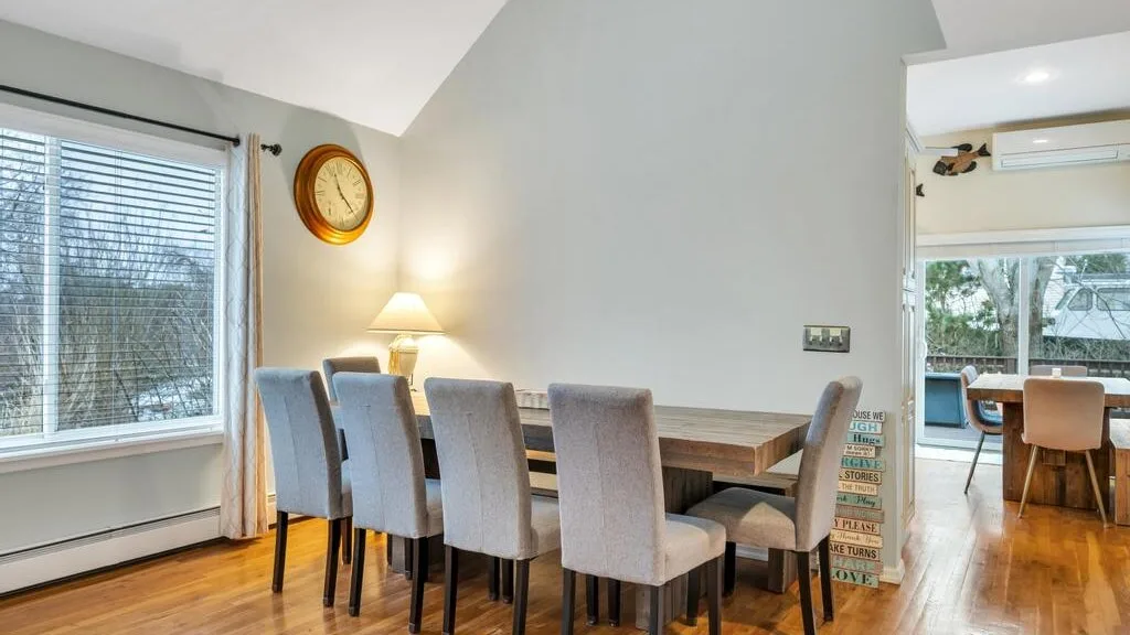 A dining area with a long table and upholstered seating beside large windows.