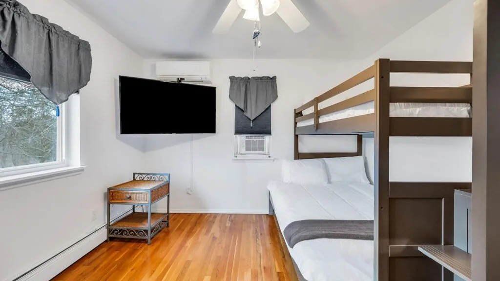 A bright bedroom with a wooden bunk bed, a wall-mounted television, and a window.