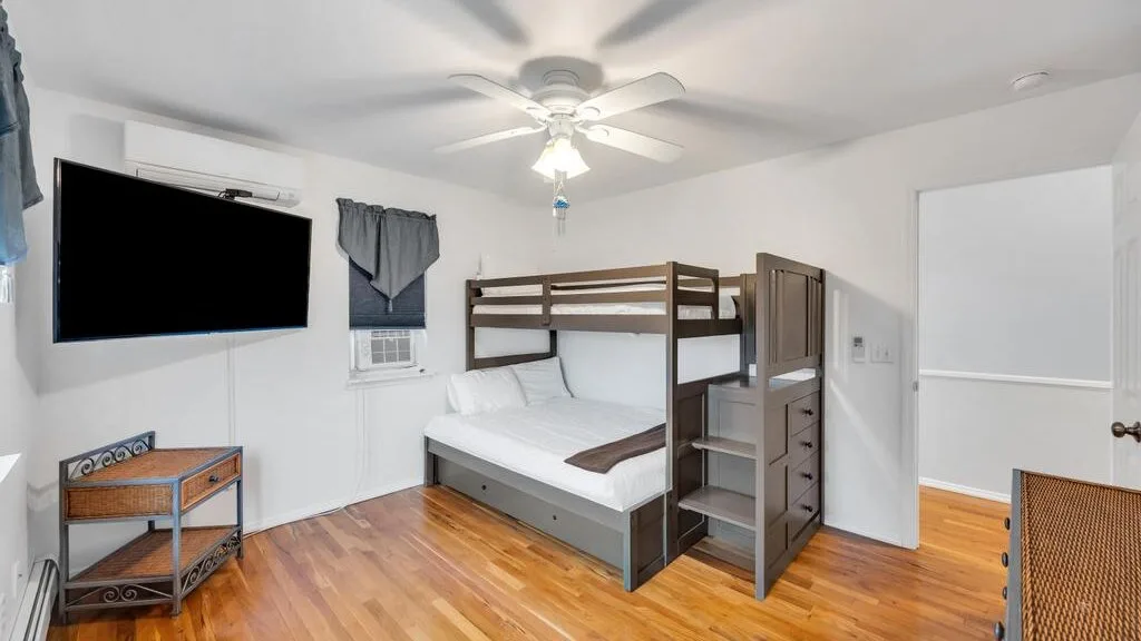 A bedroom with a bunk bed, wall-mounted television, and wooden floor.