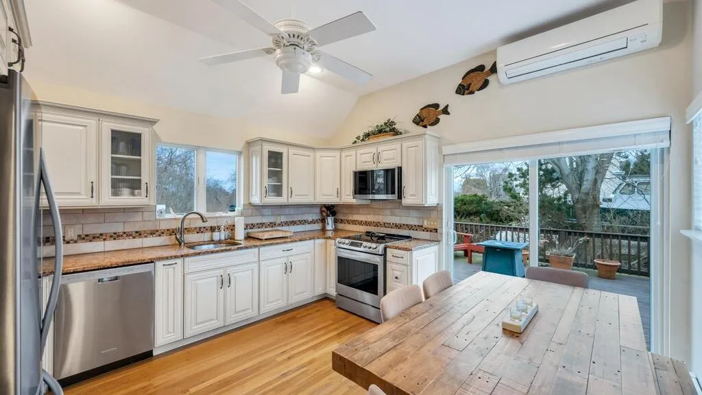 A bright kitchen with white cabinets, a wooden dining table, and sliding glass doors.