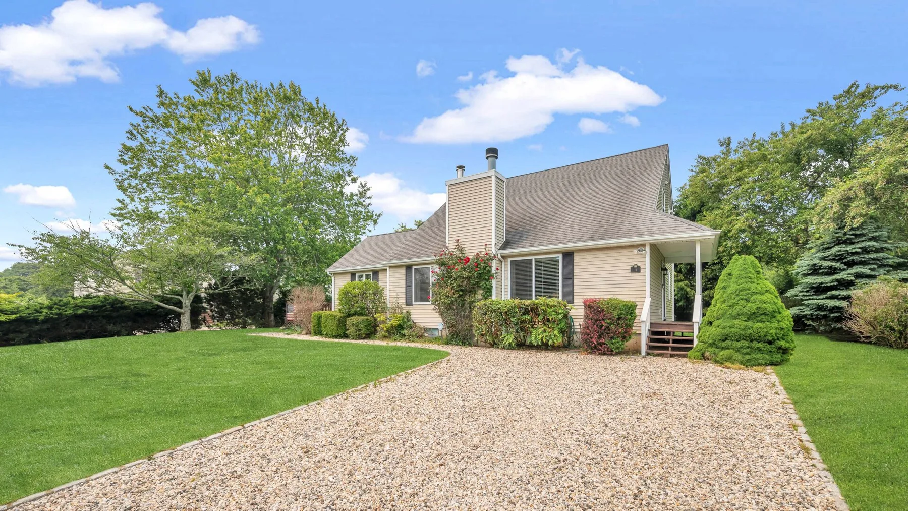 A suburban house stands beside a broad gravel driveway and green lawn.