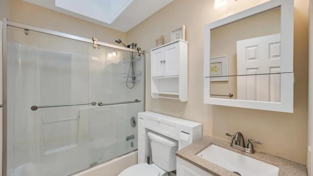 A bathroom with a glass shower, vanity, and large wall mirror.