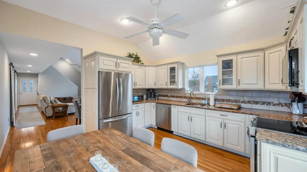 A bright kitchen with white cabinets, stainless steel appliances, and a wooden dining table.