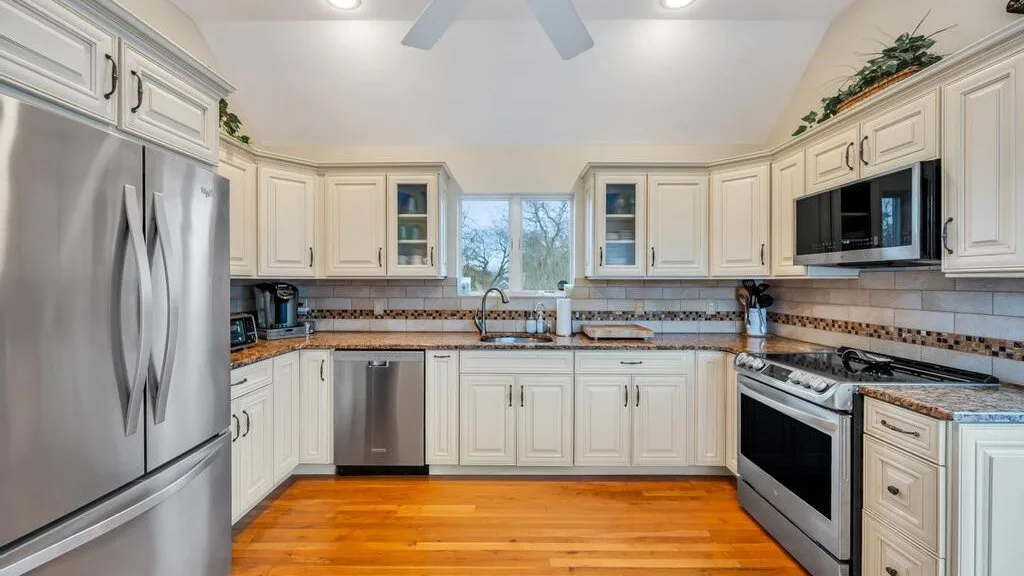 A bright kitchen with white cabinets, stainless steel appliances, and wood flooring.