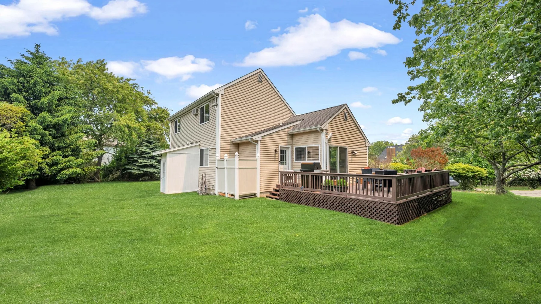 A house stands beside a broad green lawn, with a raised wooden deck.