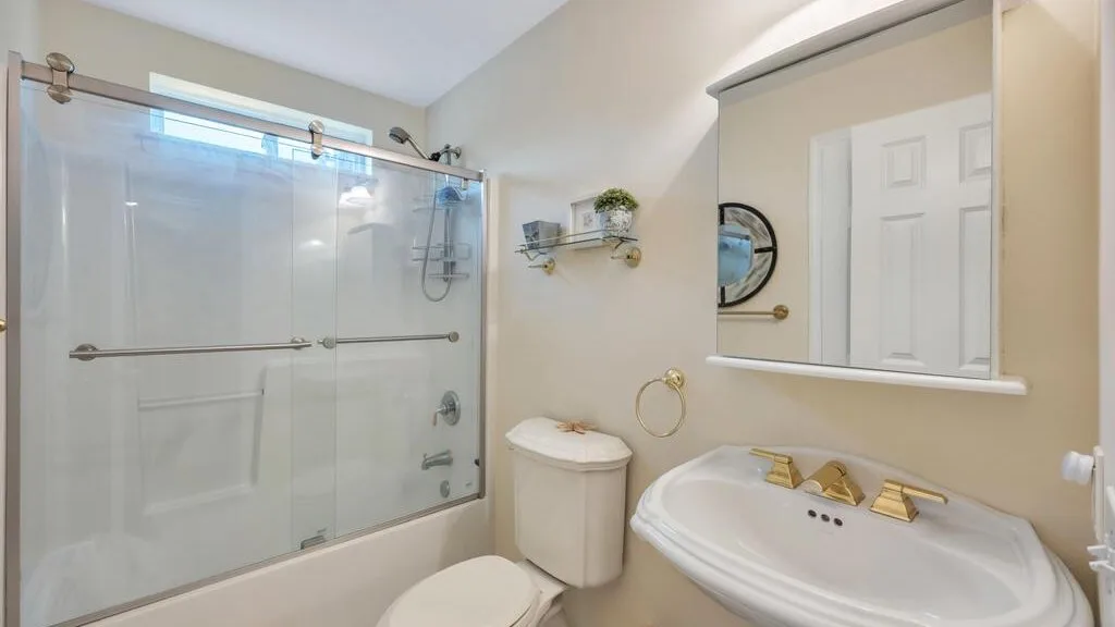 A bathroom with a glass shower, toilet, and sink.