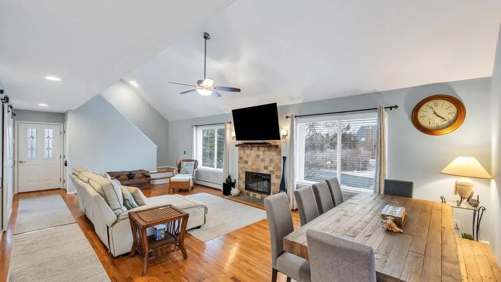 A bright living and dining room with seating, a fireplace, and a long wooden table.