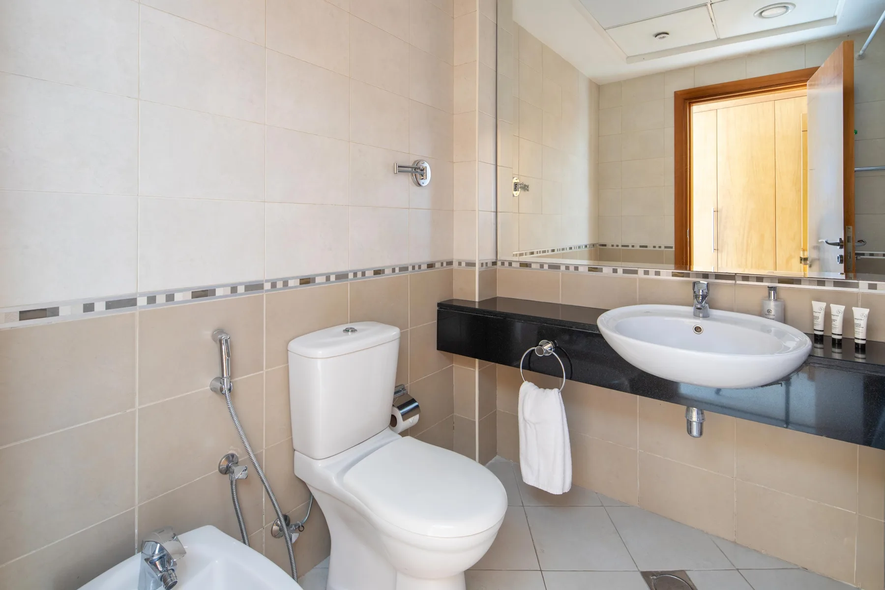 Un baño alicatado con lavabo, inodoro y un espejo amplio.