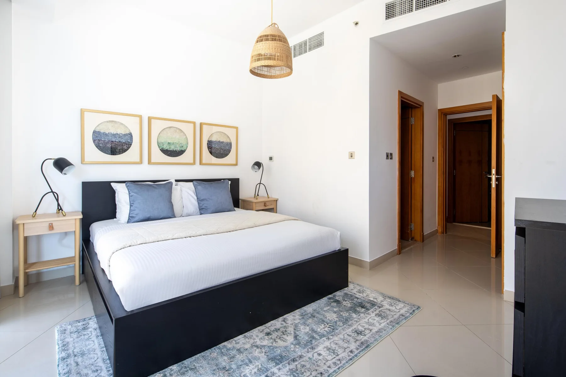 Un dormitorio luminoso con una cama tendida y cuadros enmarcados en la pared.