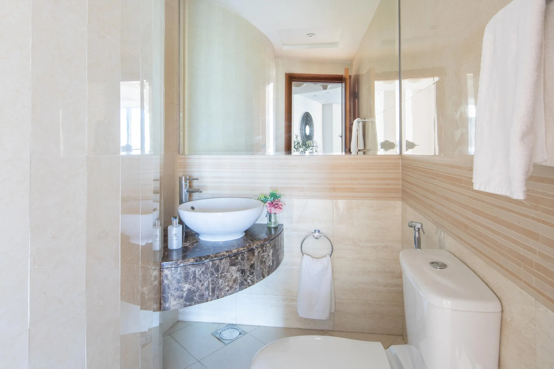 Un baño luminoso con lavabo, espejo, inodoro y toalla.