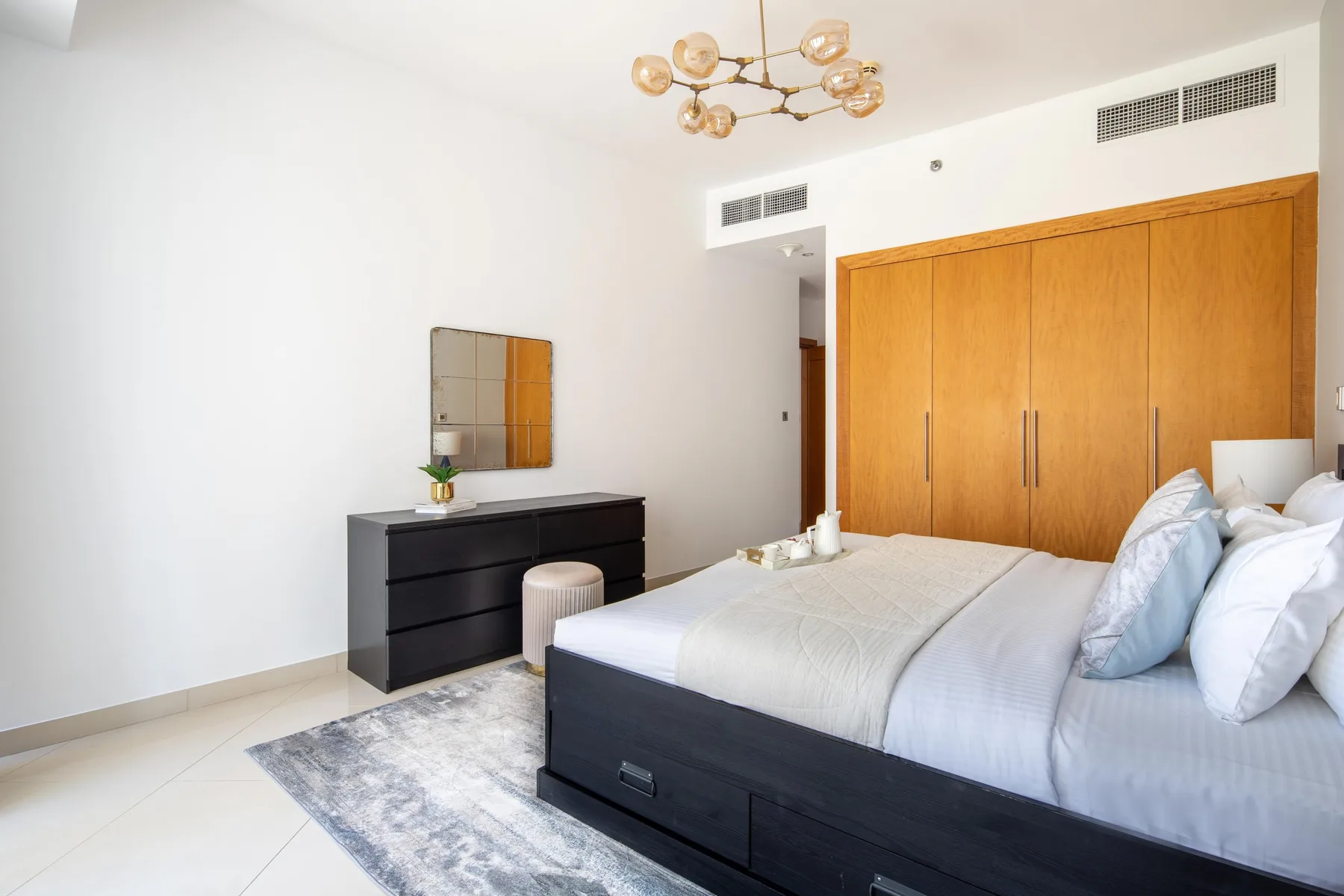Un dormitorio luminoso con una cama, armarios de madera y una cómoda oscura.
