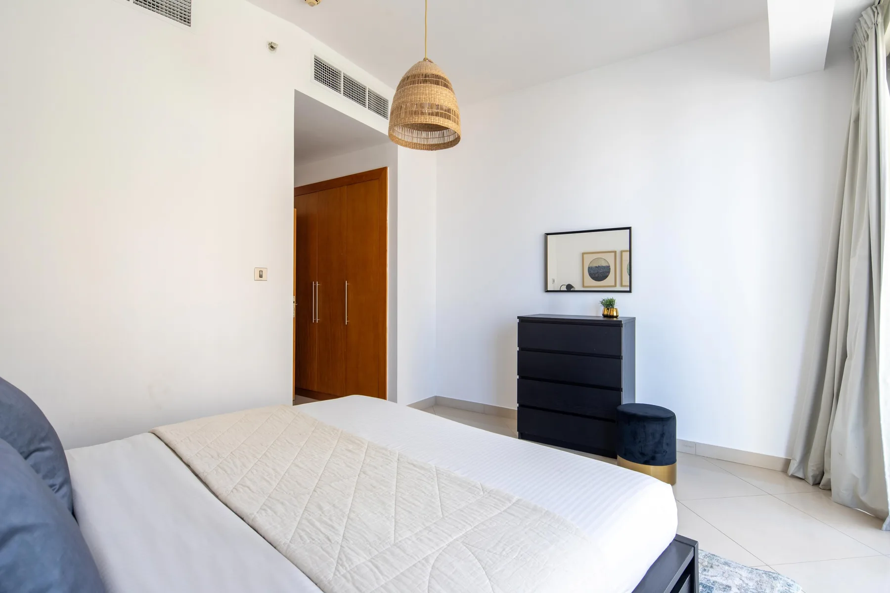 Un dormitorio luminoso con una cama bien tendida y una cómoda oscura.