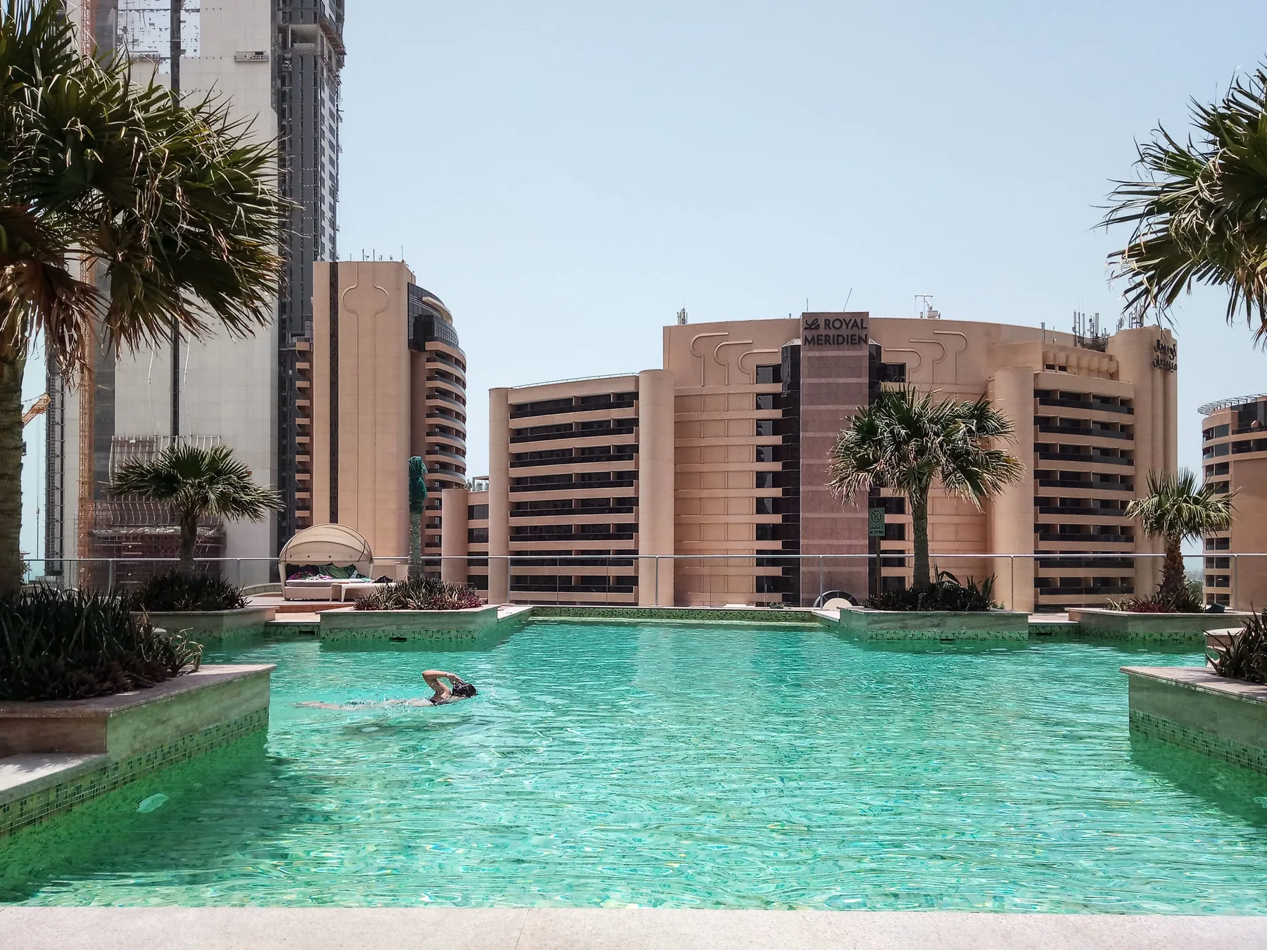 Una piscina turquesa se encuentra frente a un gran edificio hotelero y palmeras.