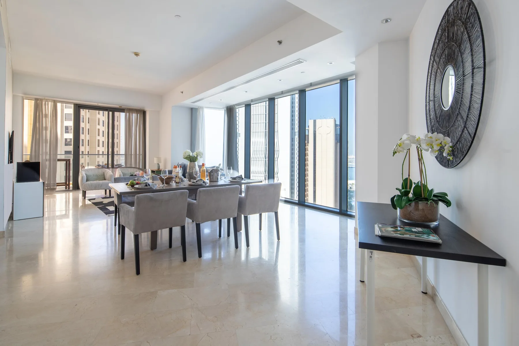 Un comedor luminoso con una mesa y grandes ventanales con vistas a edificios cercanos.