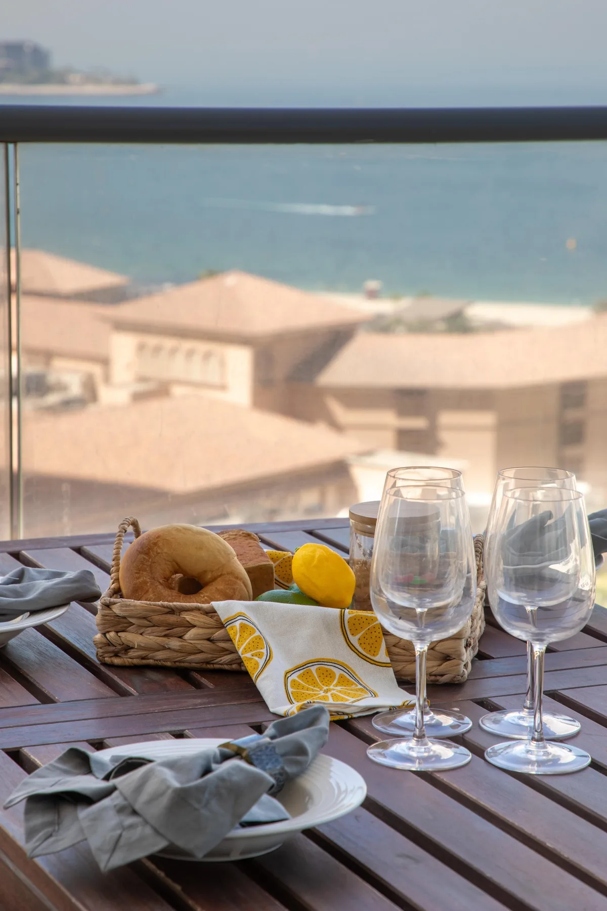 Una mesa de balcón está preparada con copas y fruta, con vistas al mar.