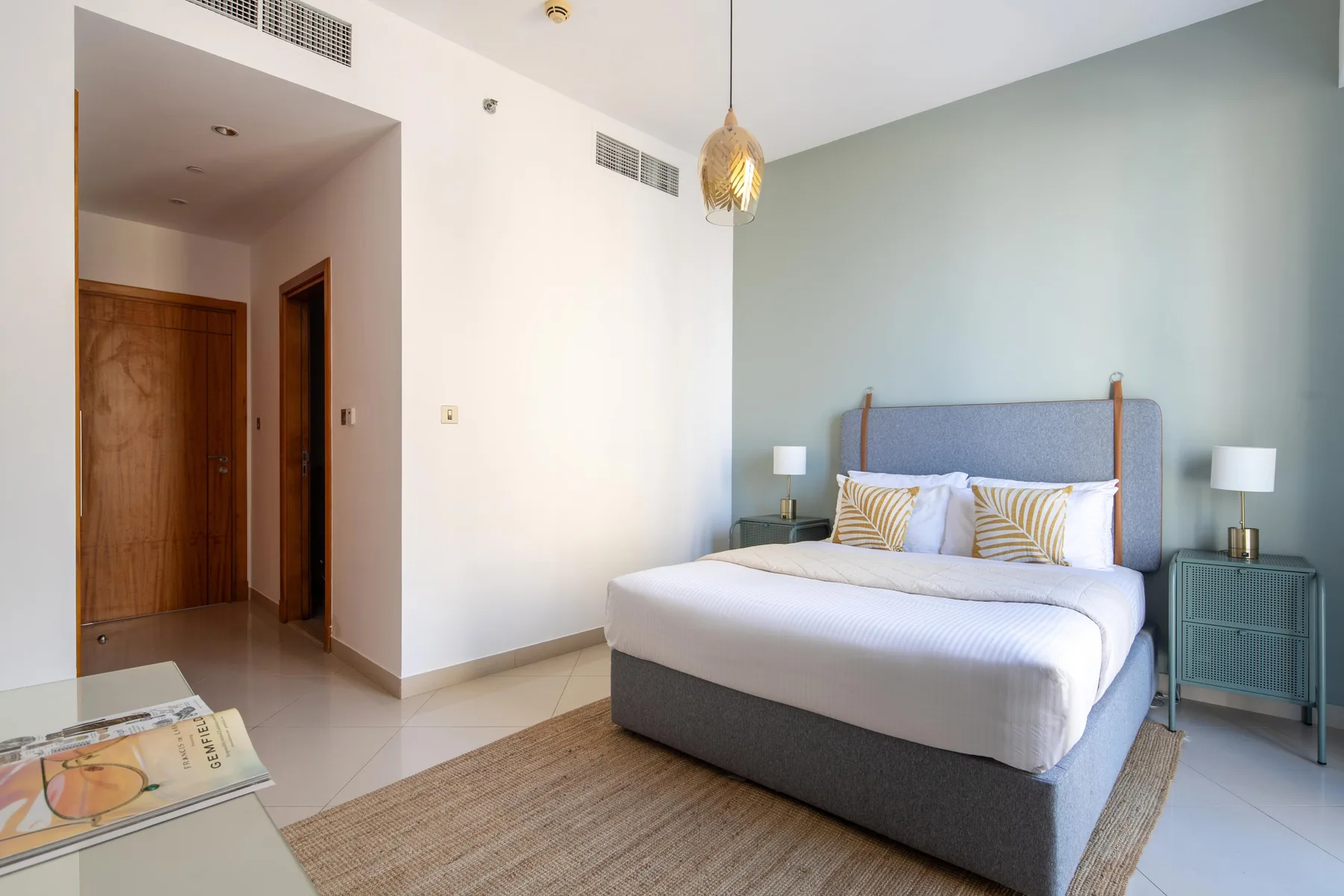 Un dormitorio con una cama bien hecha, mesas de noche y una alfombra tejida.