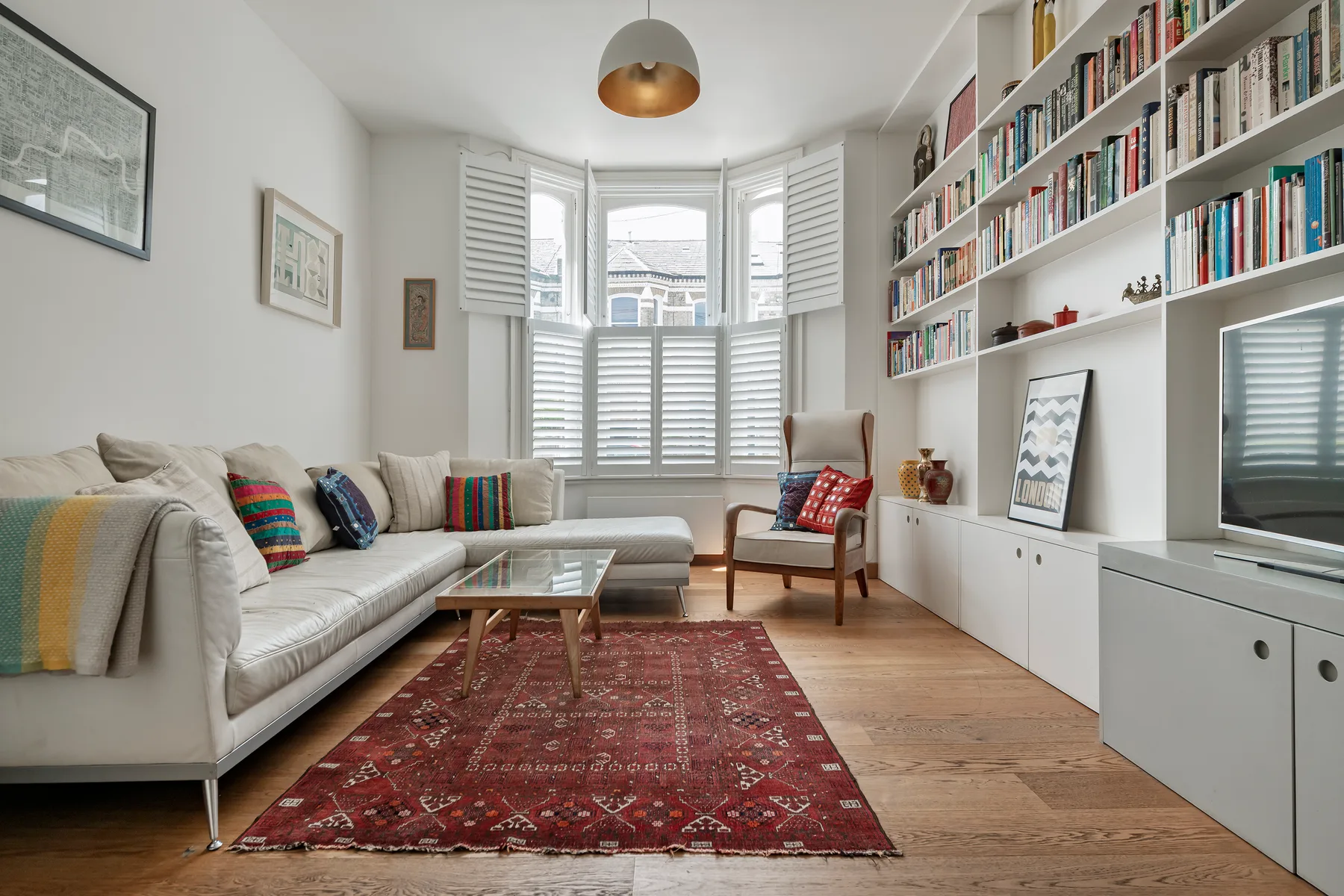 A bright living room with seating, a red patterned rug, and bookshelves.