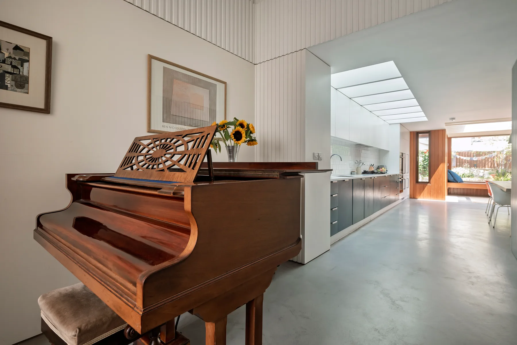 Un piano de cola está junto a una cocina abierta y luminosa con comedor.