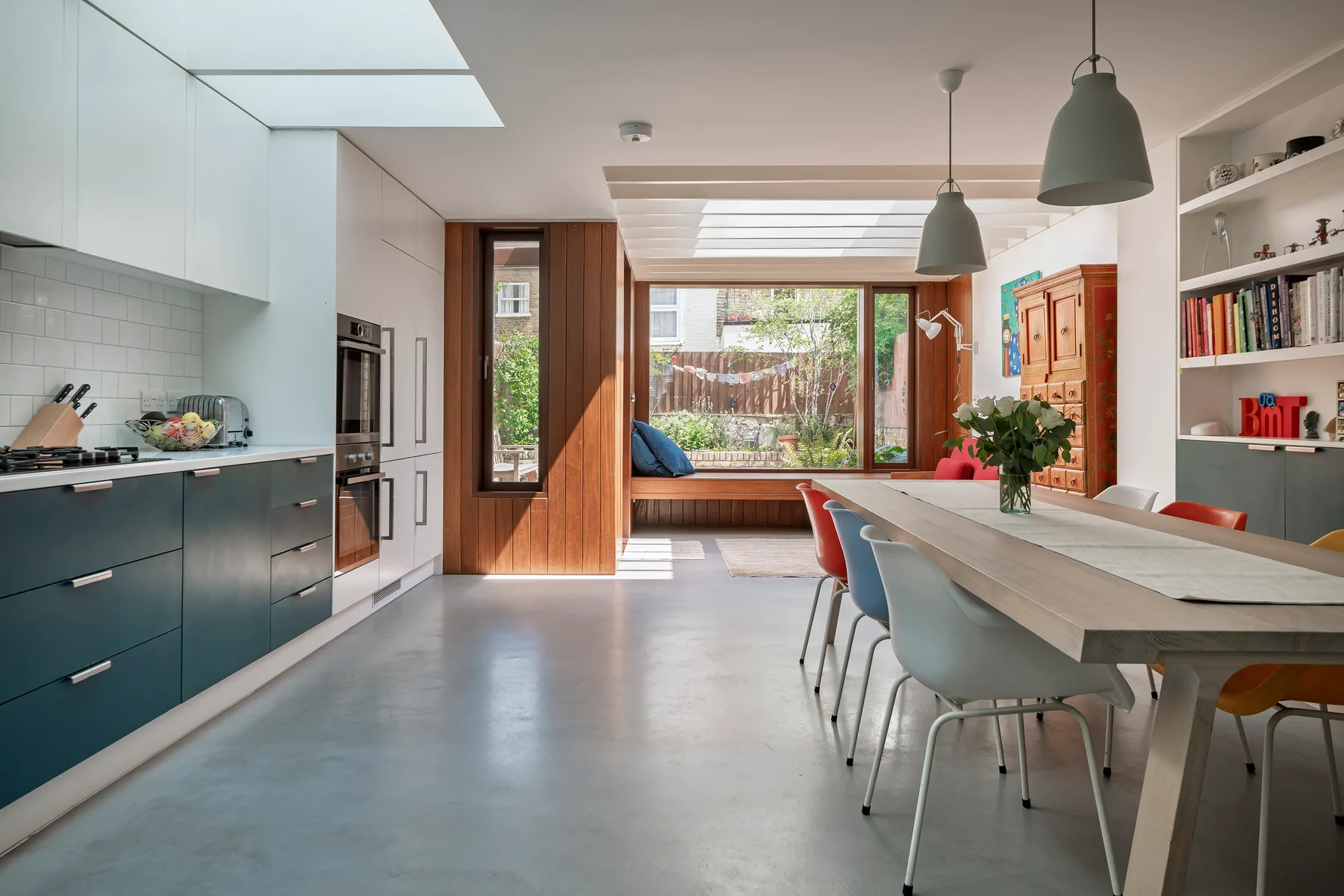 Una luminosa cocina-comedor de planta abierta con una mesa larga junto a grandes ventanas.