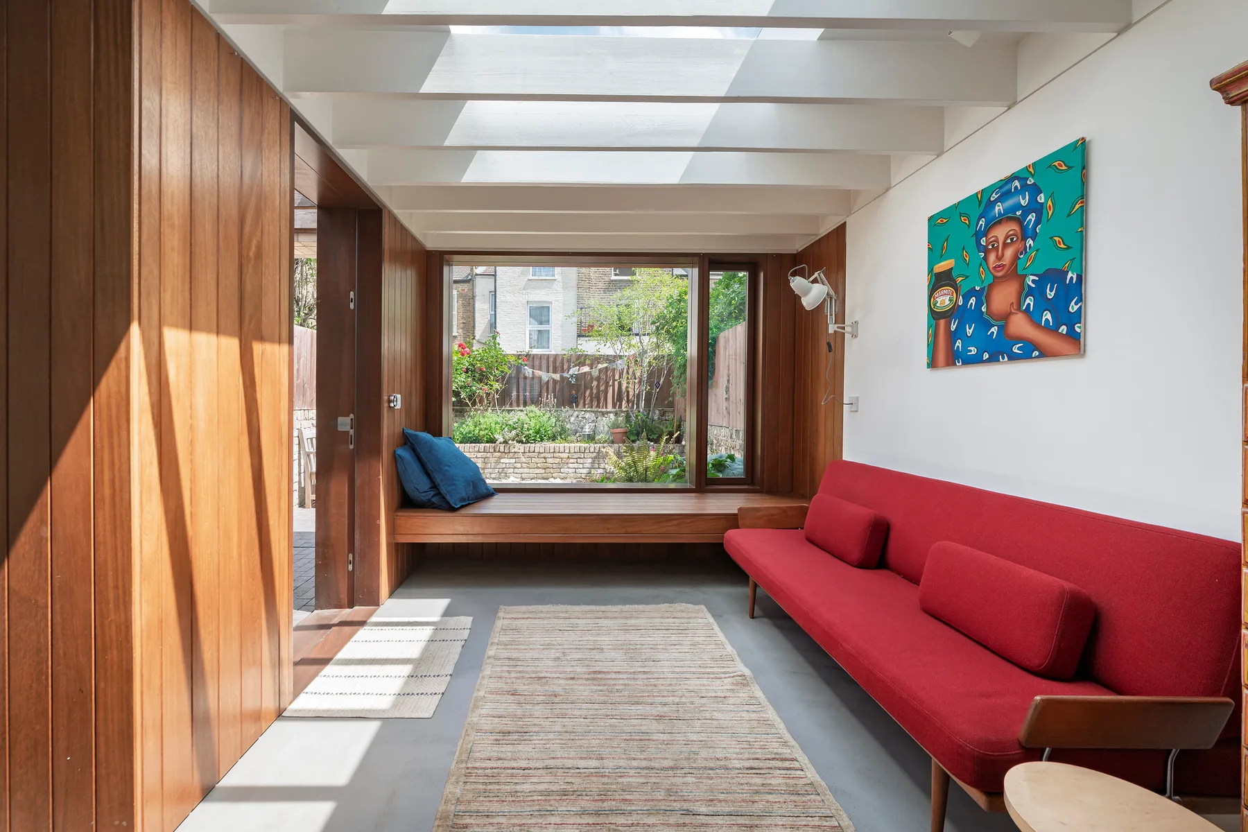 A bright living room features red seating and a large window overlooking greenery.