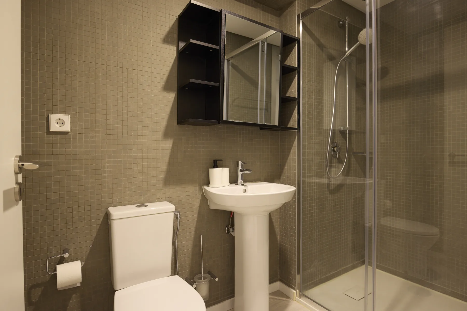 A bathroom with a toilet, pedestal sink, and glass-enclosed shower.