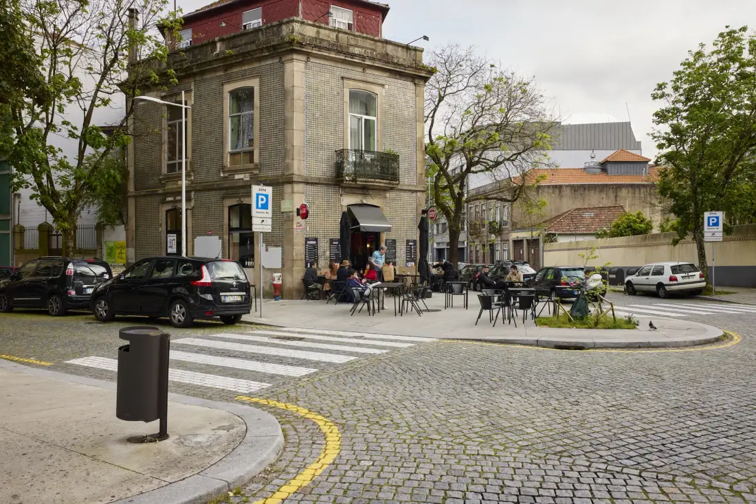 A street corner with a stone building, outdoor café seating, and parked cars.