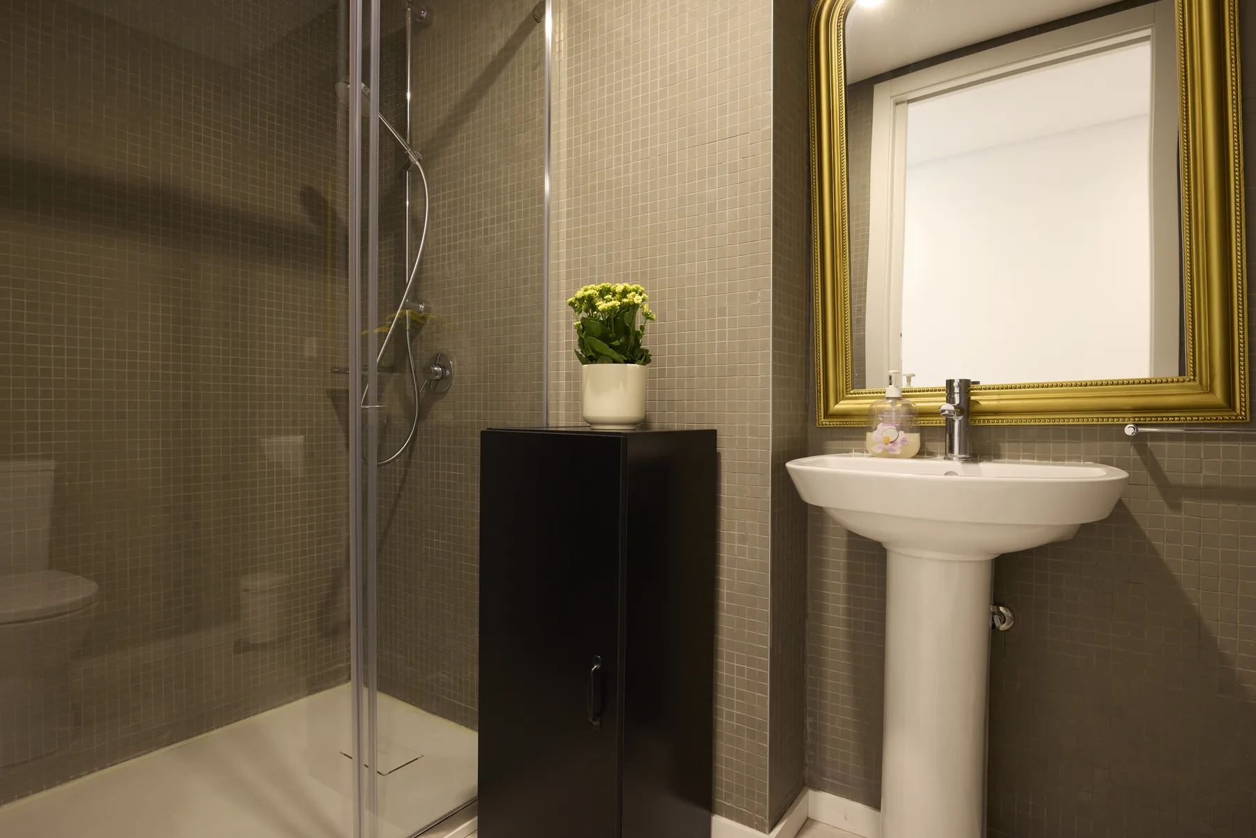 A tiled bathroom with a glass shower, pedestal sink, and wall mirror.