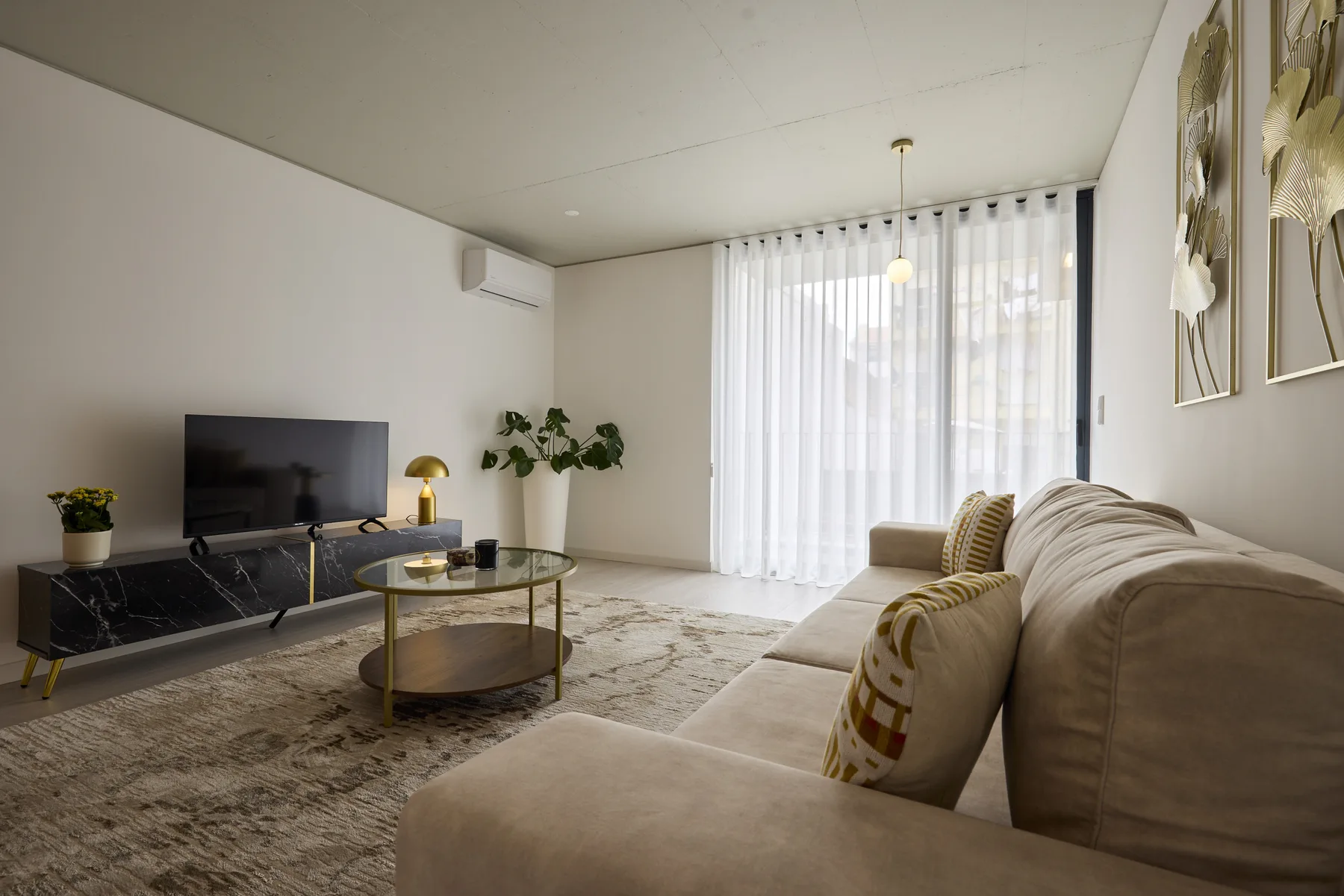 A bright living room with seating, a television, and sheer curtains.