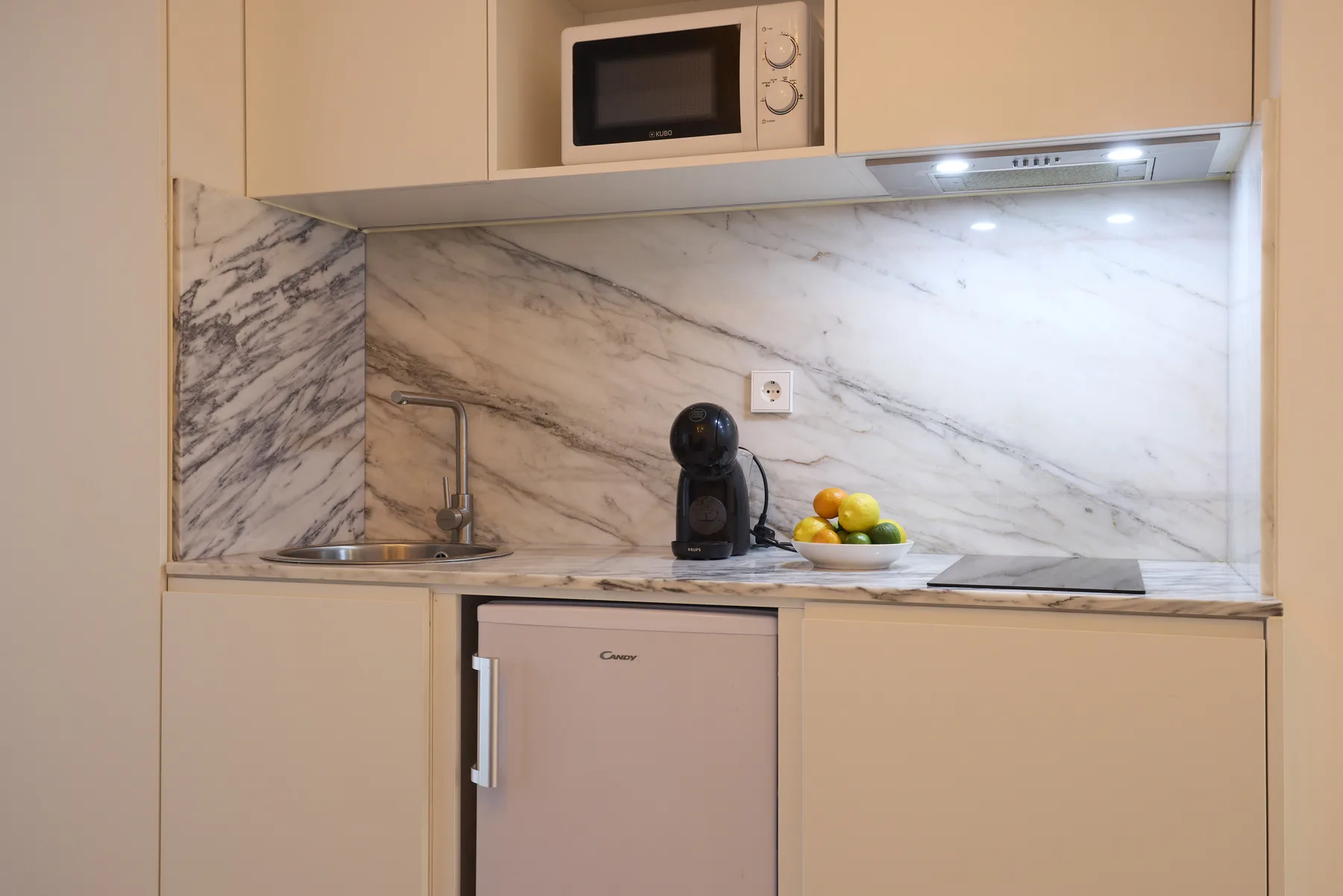 A compact kitchen with a sink, coffee machine, and fruit on the counter.