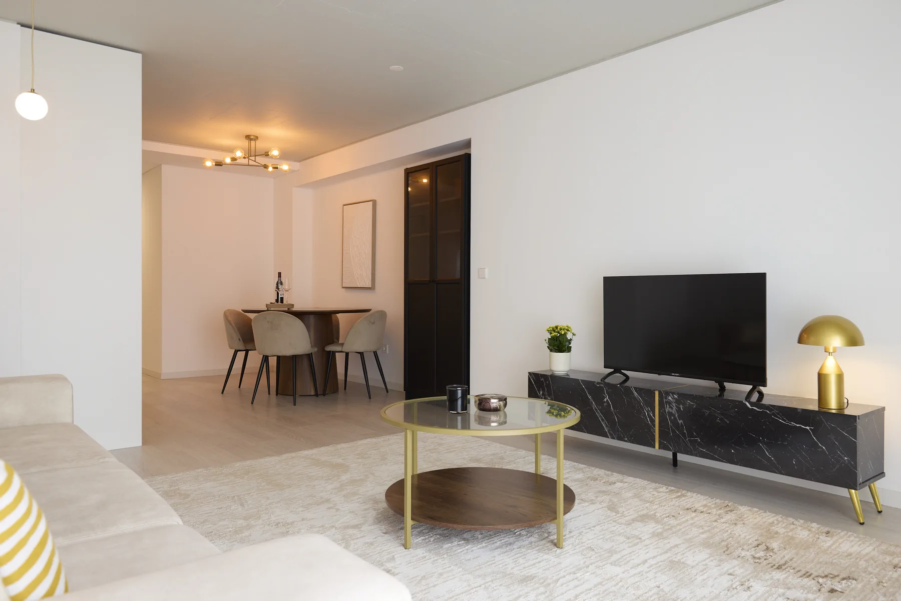 Living room with a television, coffee table, and dining area in the background.