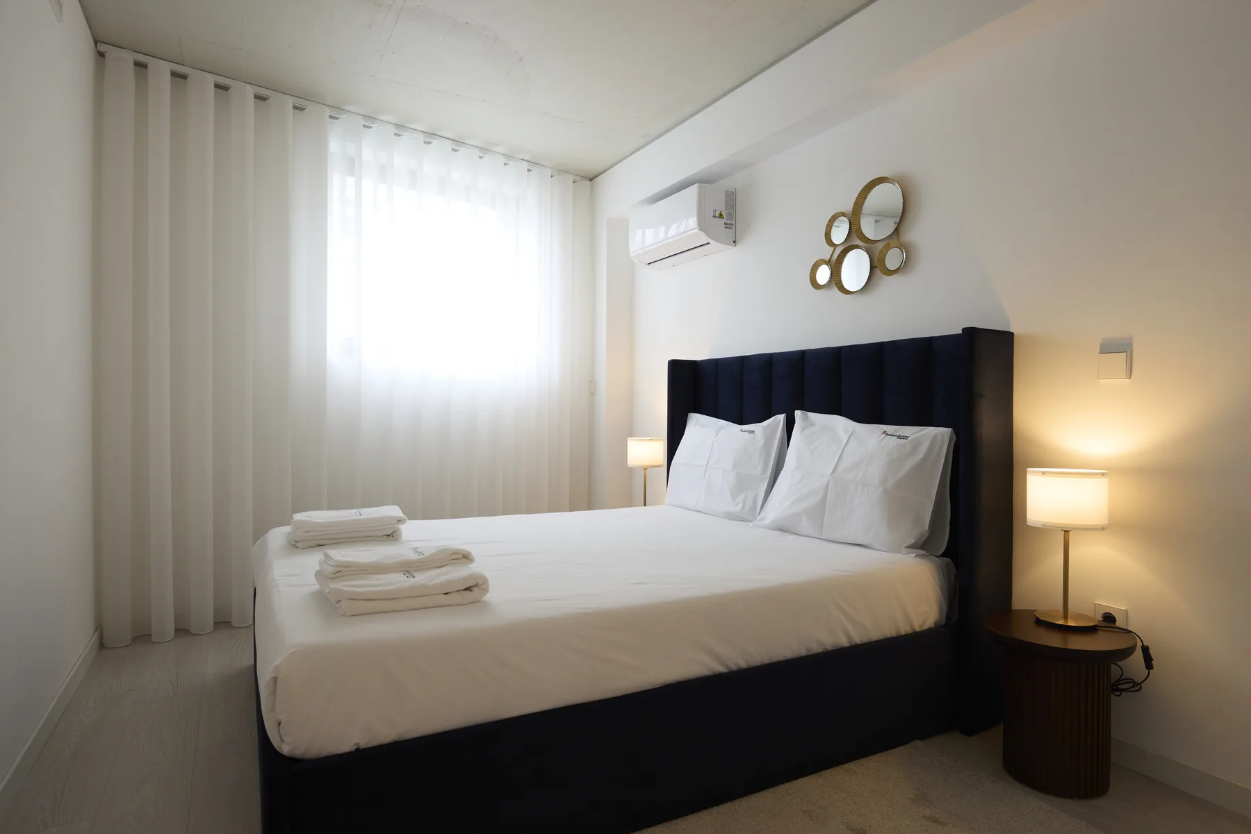 A bedroom with a bed, white bedding, and a curtained window.