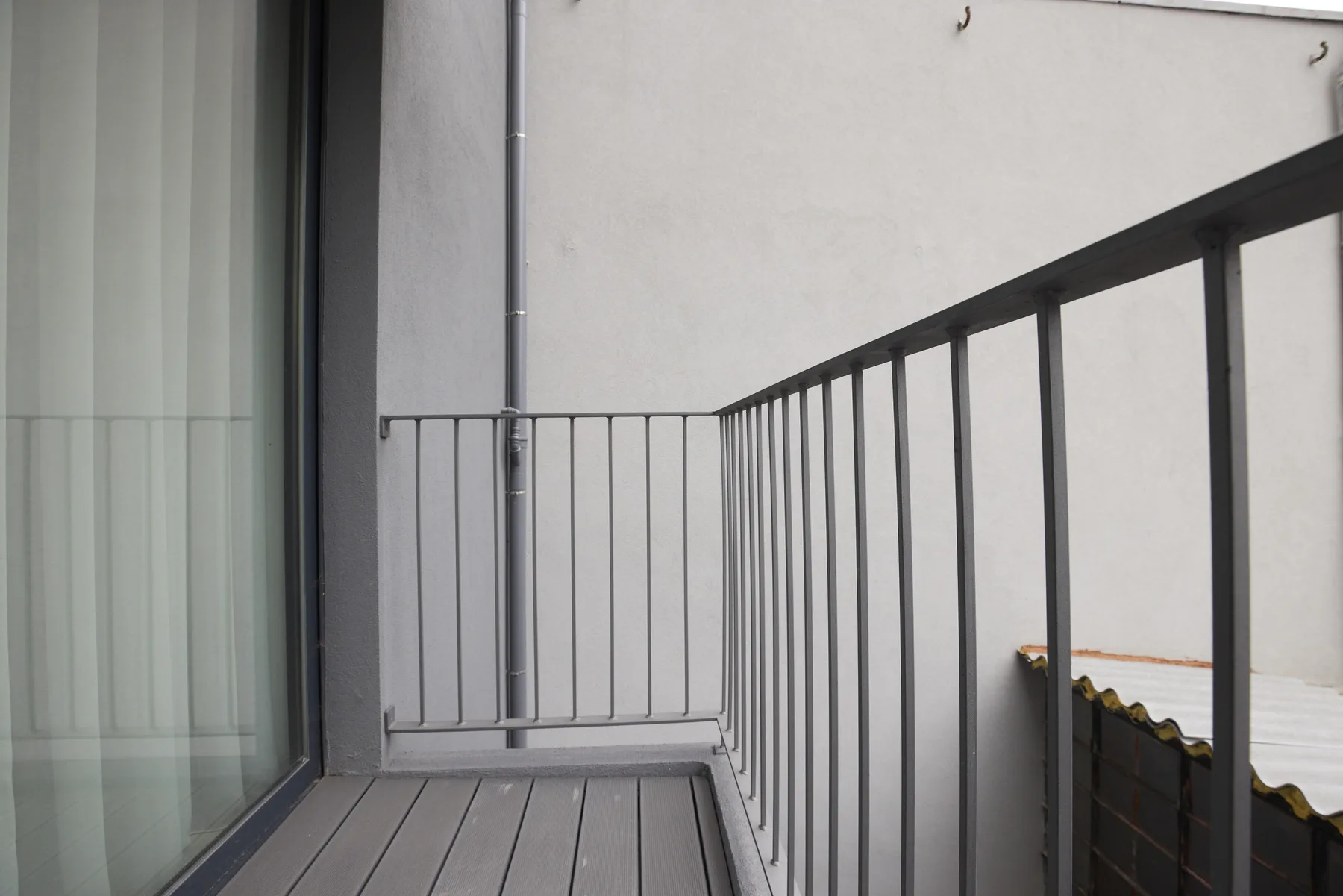 A narrow balcony with dark railings overlooks a nearby pale wall.